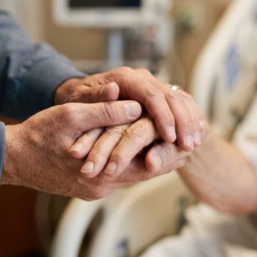 Gentle hands holding in a hospital bed, offering comfort and support to a patient La visite potentielle de Léon XIV en France et son impact sur le débat sur la fin de vie