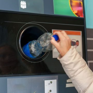 Person recycling a plastic bottle at a modern recycling station inside a city environment Les Enjeux du Réemploi contre la Consigne Plastique