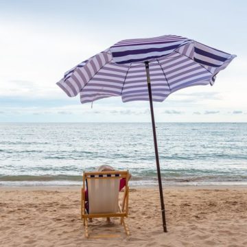 Traveler woman relax on the beach chair with umbrella at the beach. L’importance des vacances dans nos sociétés modernes
