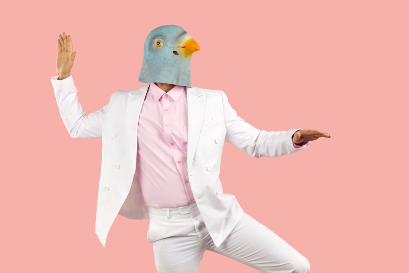 Funny man in rubber pigeon mask and in white formal suit dancing on pink background. Critique du roman L’Adolescence du perroquet par Amélie Nothomb