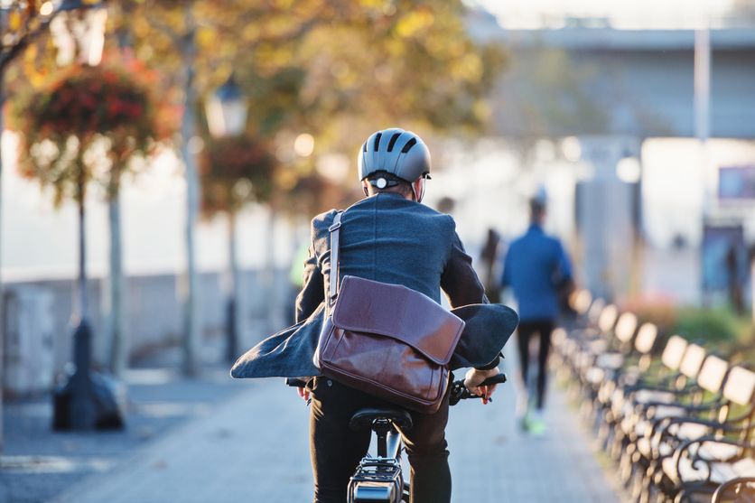 A rear view of businessman commuter with electric bicycle traveling to work in city. Débat sur l’Obligation du Casque pour Cyclistes