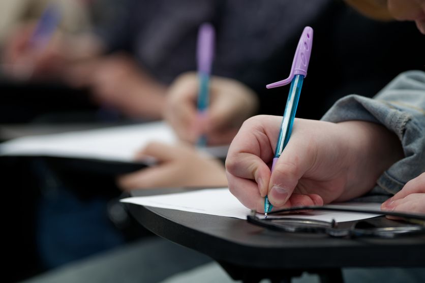 Group of students taking a test at their desks. Selective focus on a hand holding a pen over a blank sheet. Ideal for university lectures, homework, and diligence themes. Photo Le parcours contesté du questionnaire sur les violences sexistes et sexuelles en milieu scolaire